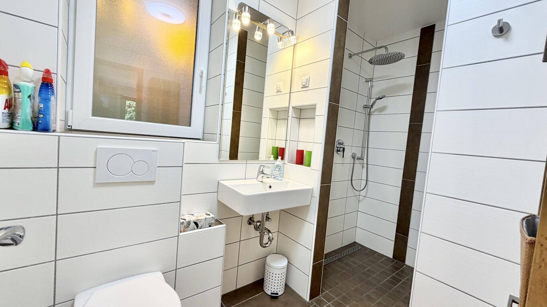 Modern gefliestes Badezimmer mit ebenerdiger Dusche, Waschbecken und Fenster für Tageslicht.
