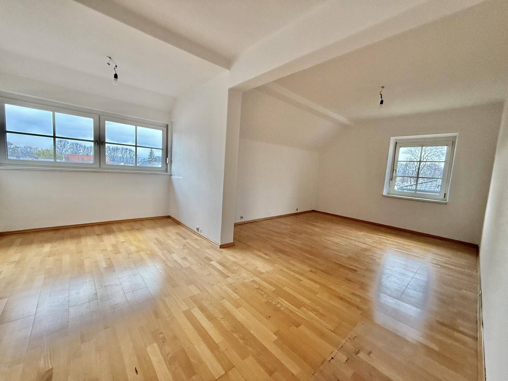 Helles Zimmer im Dachgeschoss mit Holzboden, Dachschrägen und zwei Fenstern.
