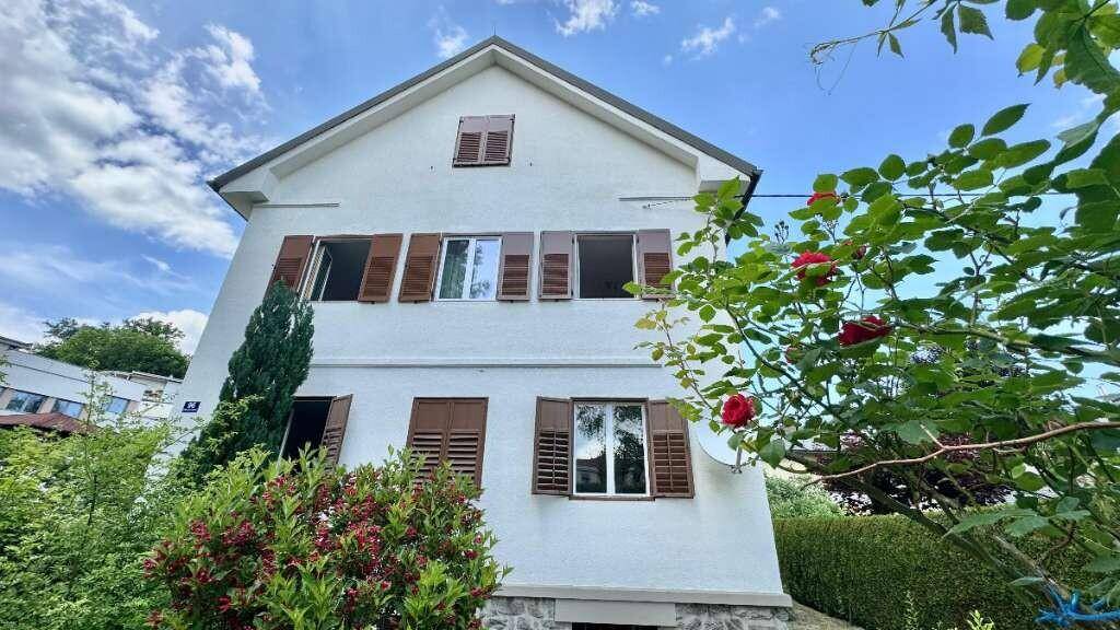 Fassade des Hauses mit Fensterläden und blühenden Sträuchern im Vorgarten.