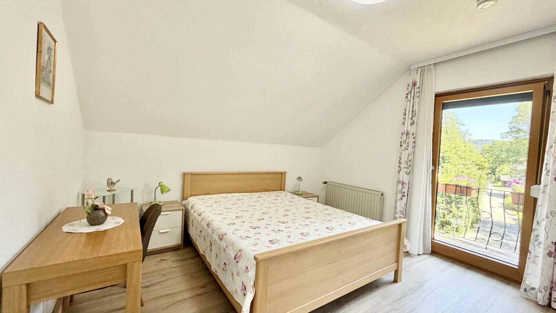 Helles Schlafzimmer im Dachgeschoss mit Doppelbett, Schreibtisch und Zugang zum Balkon.