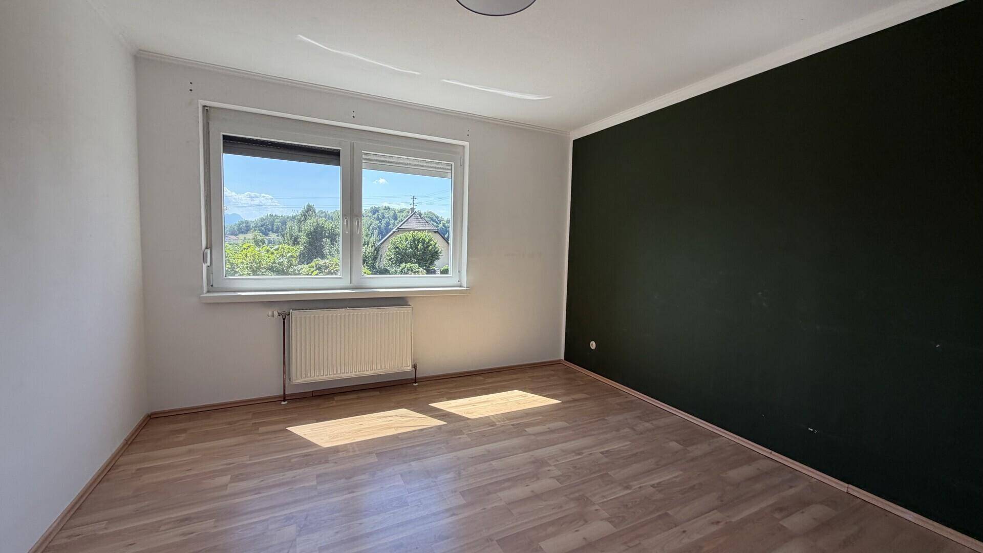 Schlafzimmer mit Holzboden und dunkler Akzentwand, hell durch Fenster.