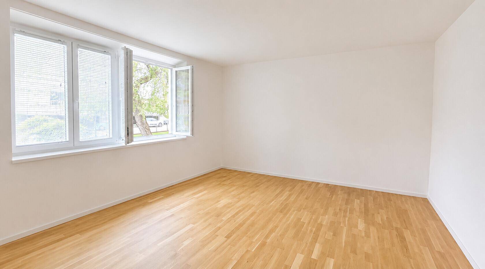 Leerer Raum mit großen Fenstern und hellem Parkettboden, bereit zur individuellen Gestaltung.