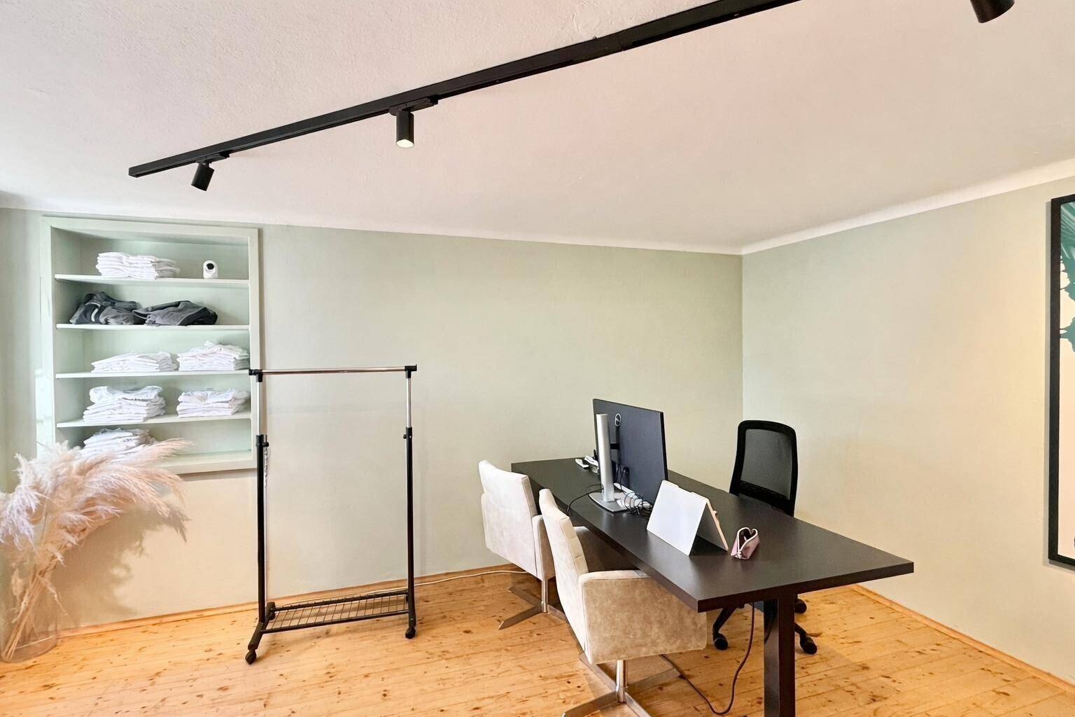 Funktionales Büro mit hellem Holzfußboden, eingebautem Regal und moderner Beleuchtung.