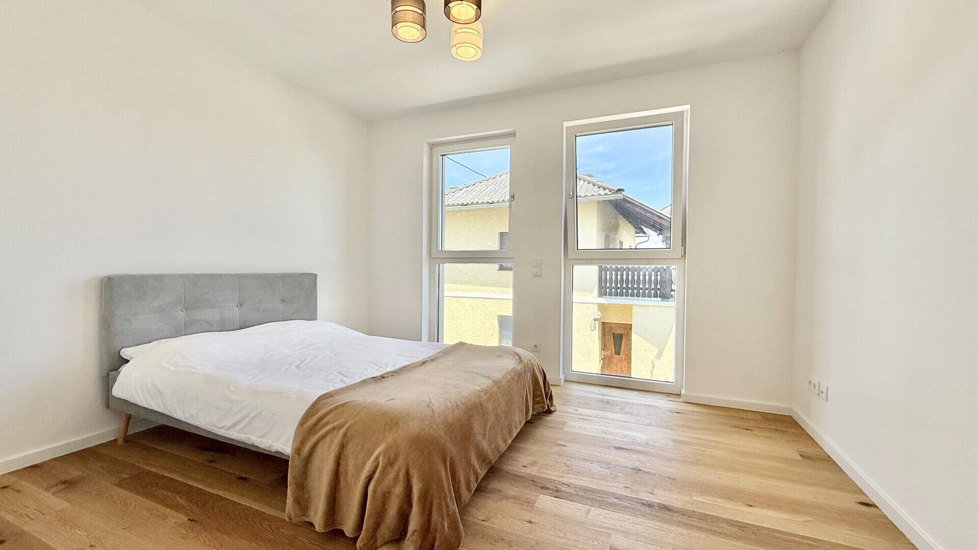Helles Schlafzimmer mit Holzboden, großem Fenster und einem modernen Bett mit einfacher Dekoration.