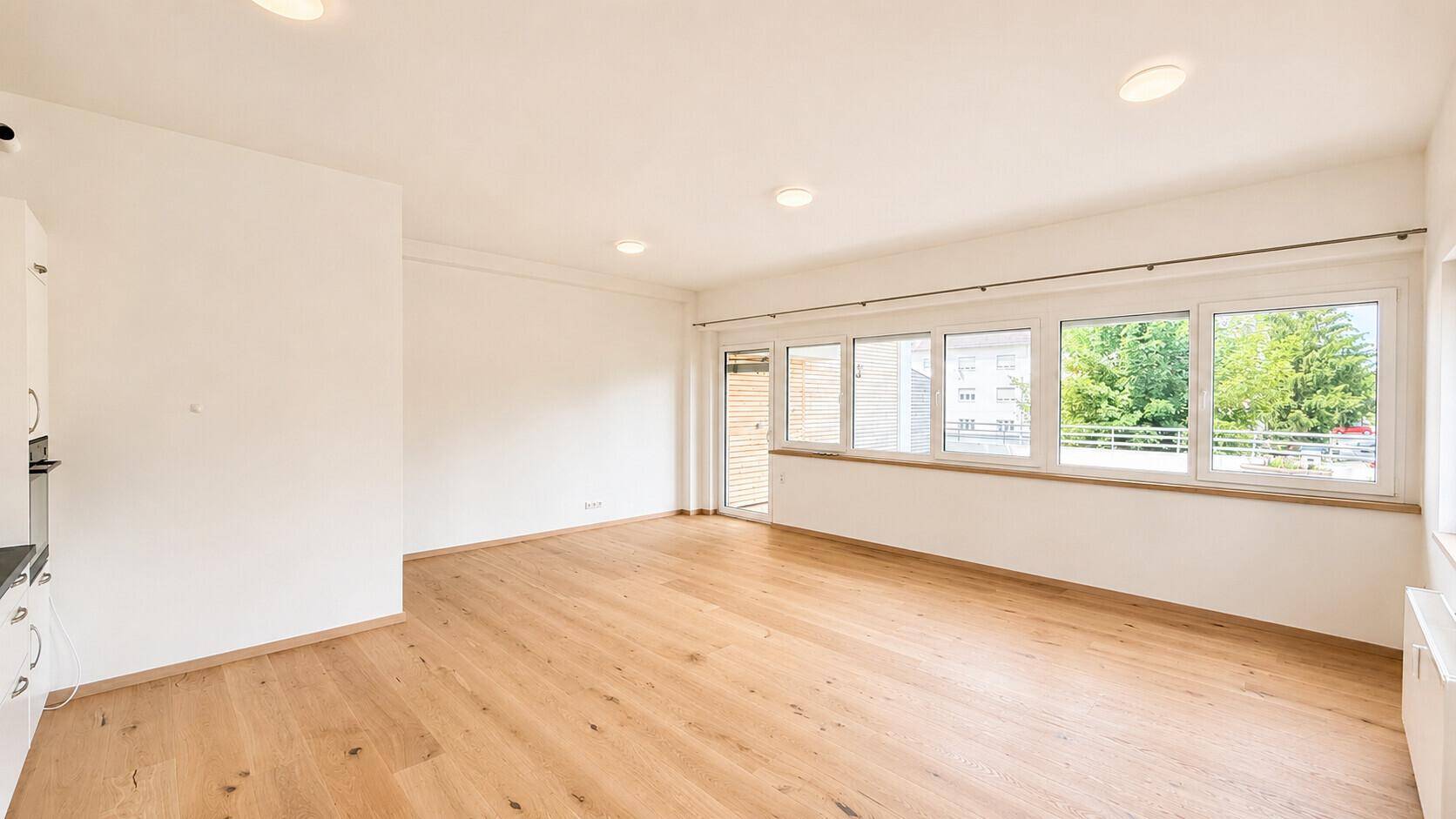 Lichtdurchfluteter Wohnbereich mit hellem Holzboden und Zugang zu einem Außenbereich durch große Fenster.