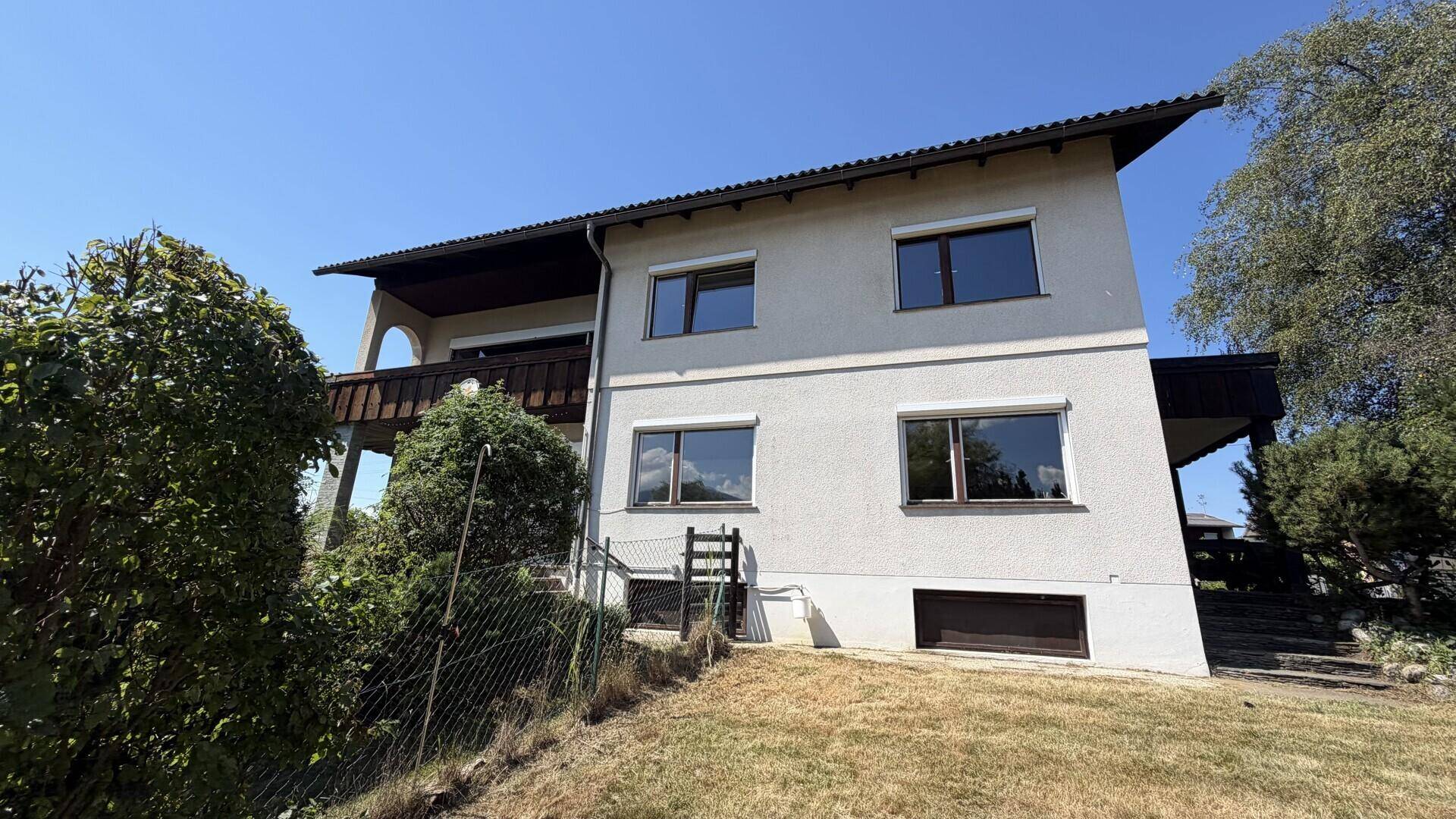 Ansicht des Hauses von außen mit Balkon und Gartenbereich unter blauem Himmel.