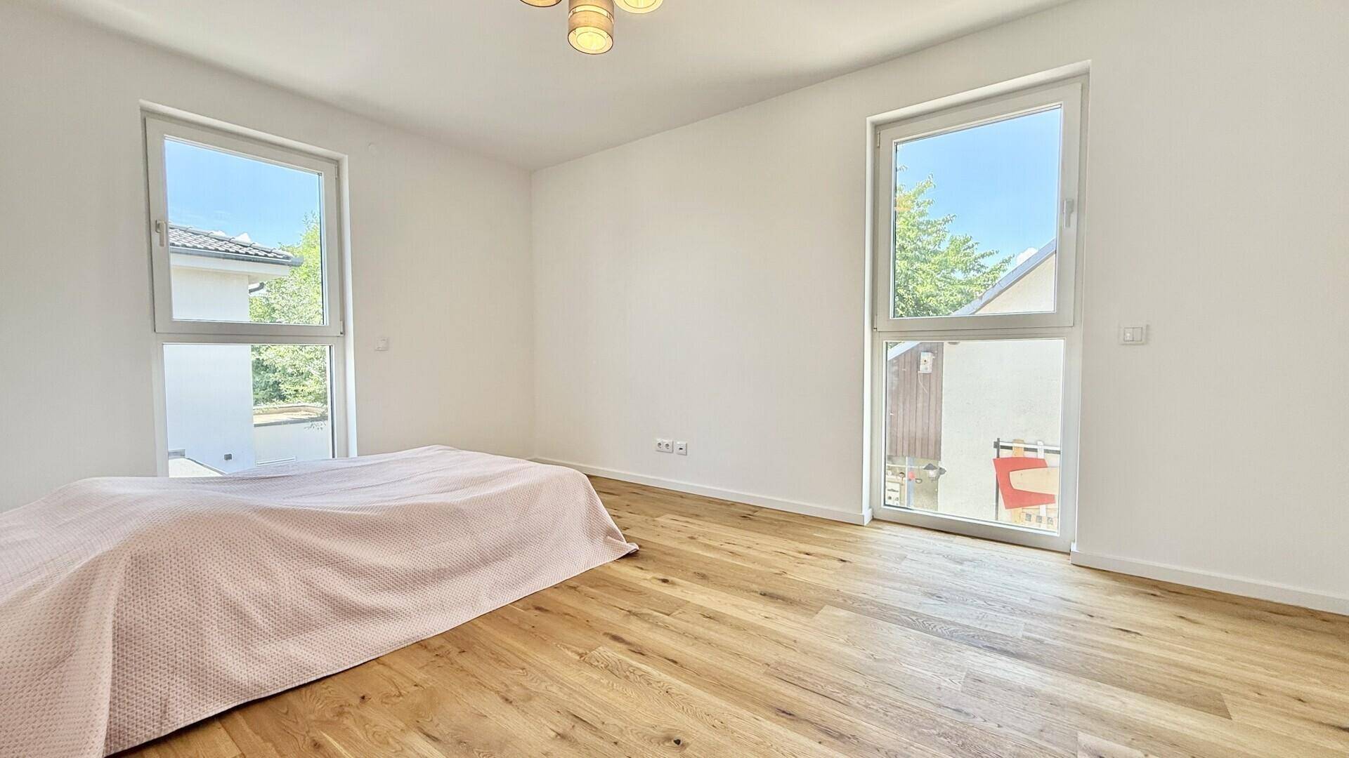 Geräumiges Schlafzimmer mit Holzboden und zwei großen Fenstern, die viel Tageslicht hereinlassen.