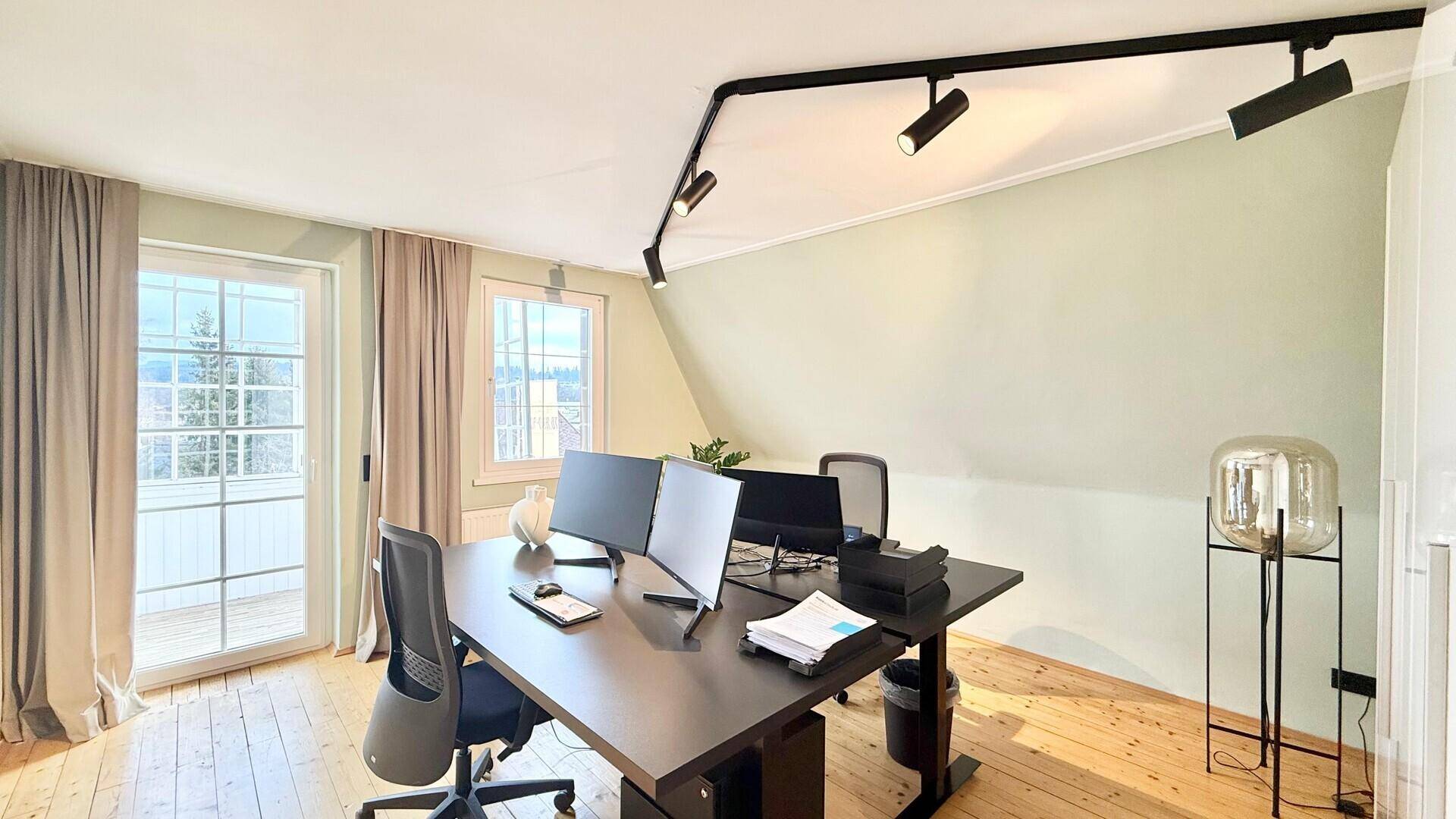 Geräumiges Büro mit mehreren Arbeitsplätzen, Holzboden und Zugang zu einem Balkon.