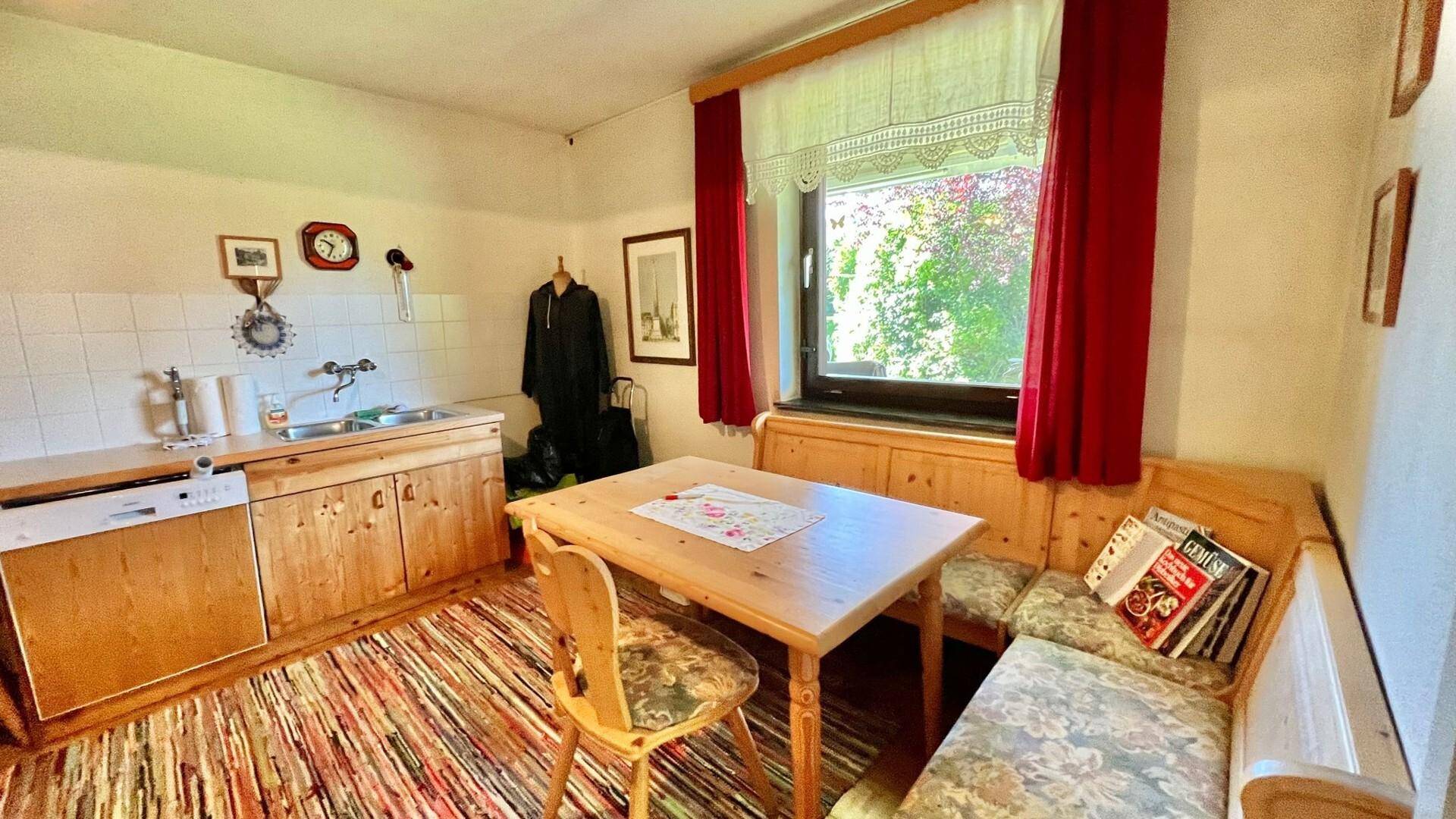 Gemütliche Küche mit Holzelementen, Essbereich und Fenster mit rotem Vorhang.