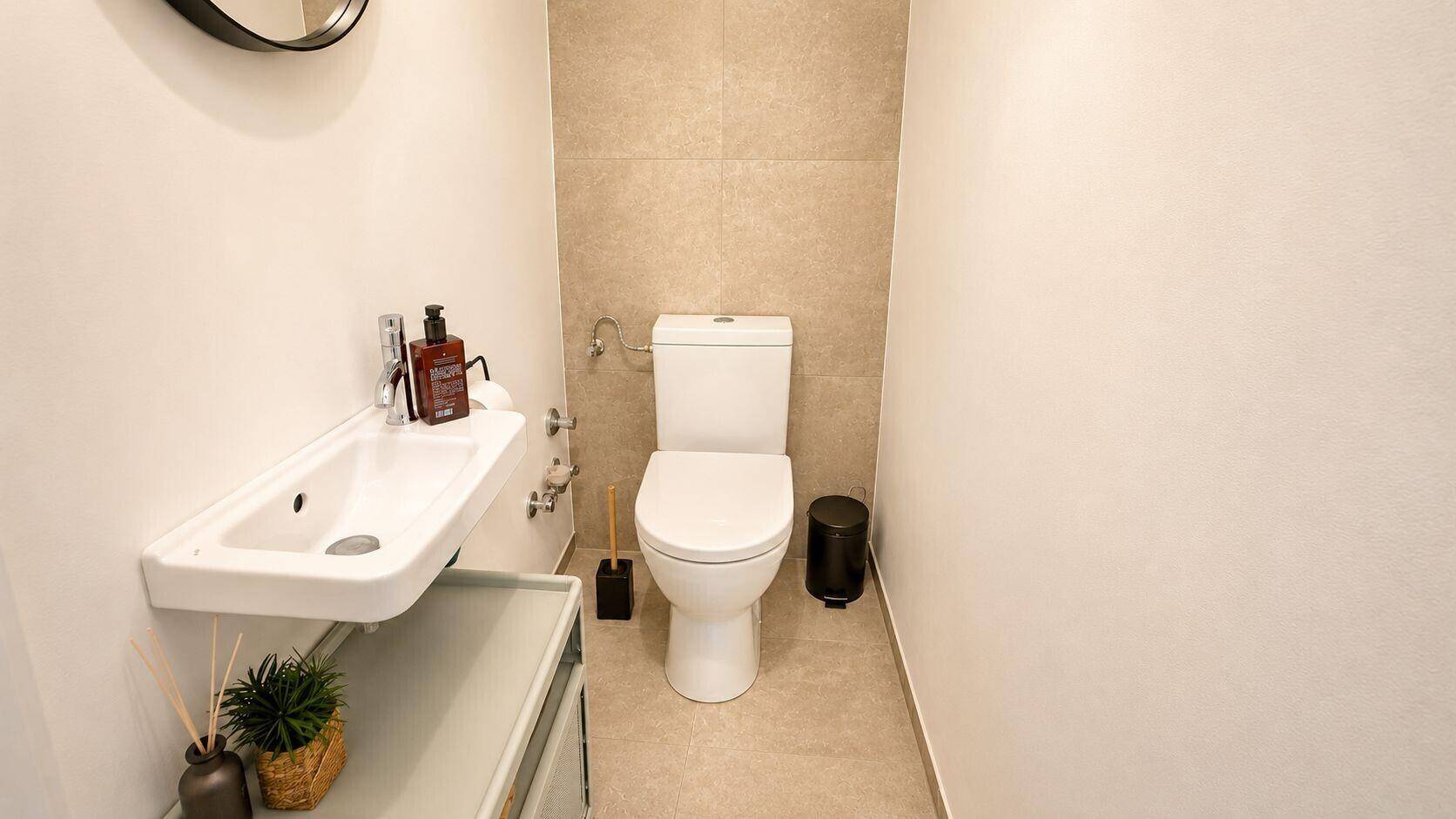 Modernes Gäste-WC mit Wand-WC, kleinem Waschbecken und beigen Fliesen.