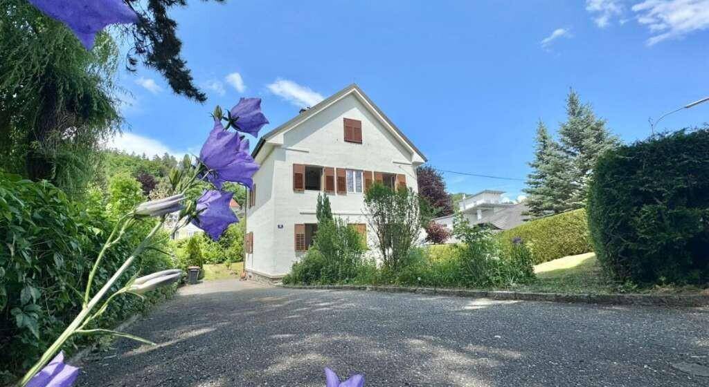 Vorderansicht des weißen Hauses mit braunen Fensterläden und gepflasterter Zufahrt.