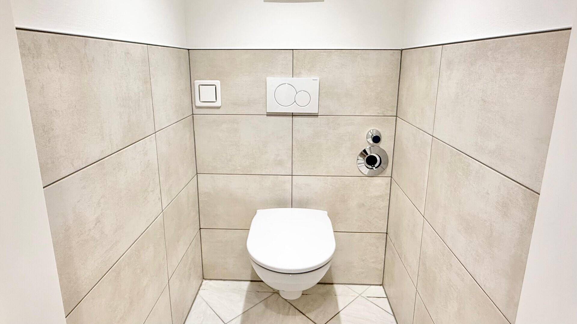 Modernes WC mit wandhängender Toilette und beigefarbenen Großformatfliesen an den Wänden.