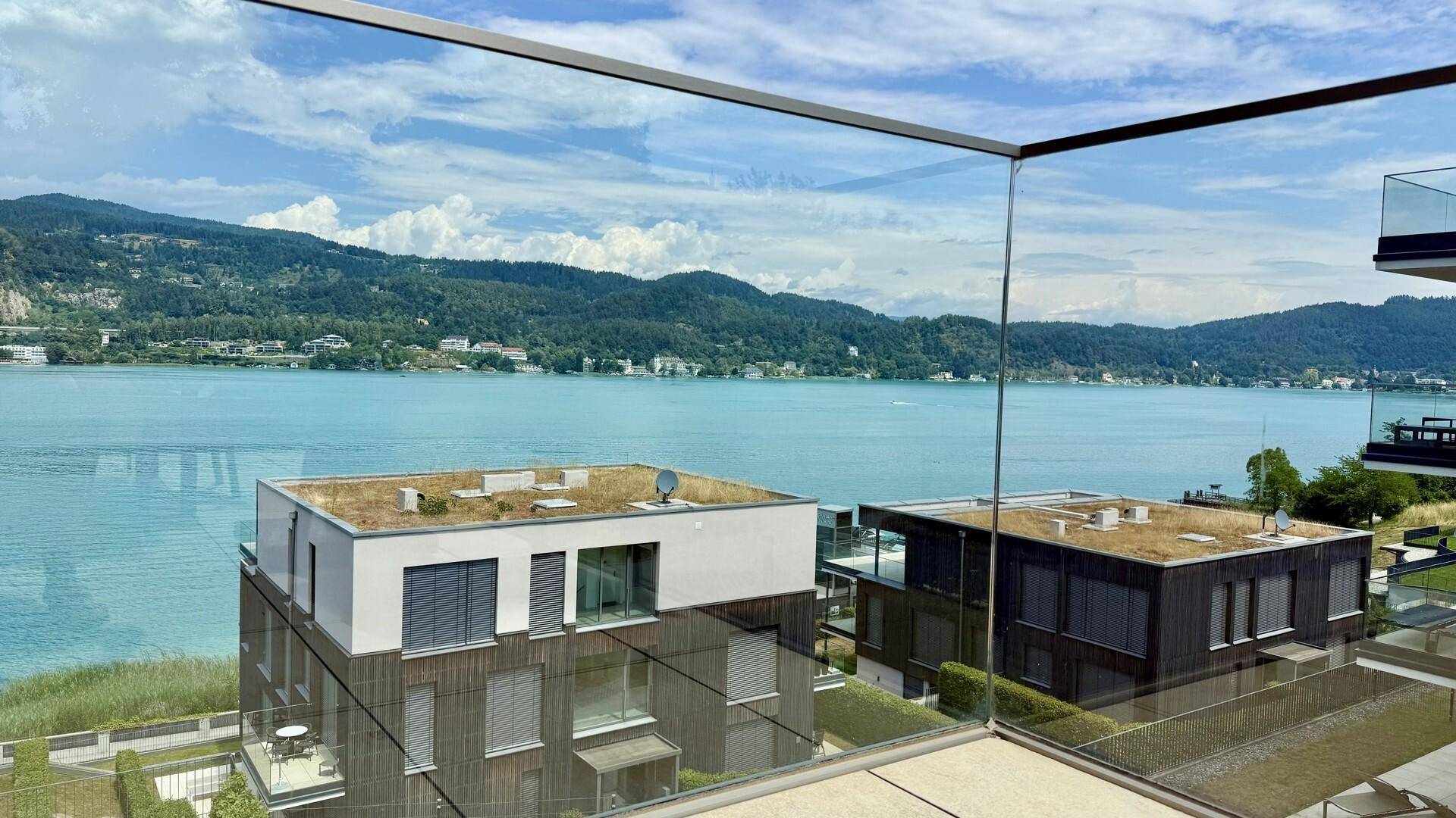 Panoramablick von der Terrasse auf den glitzernden See, die Berge und moderne Architektur.