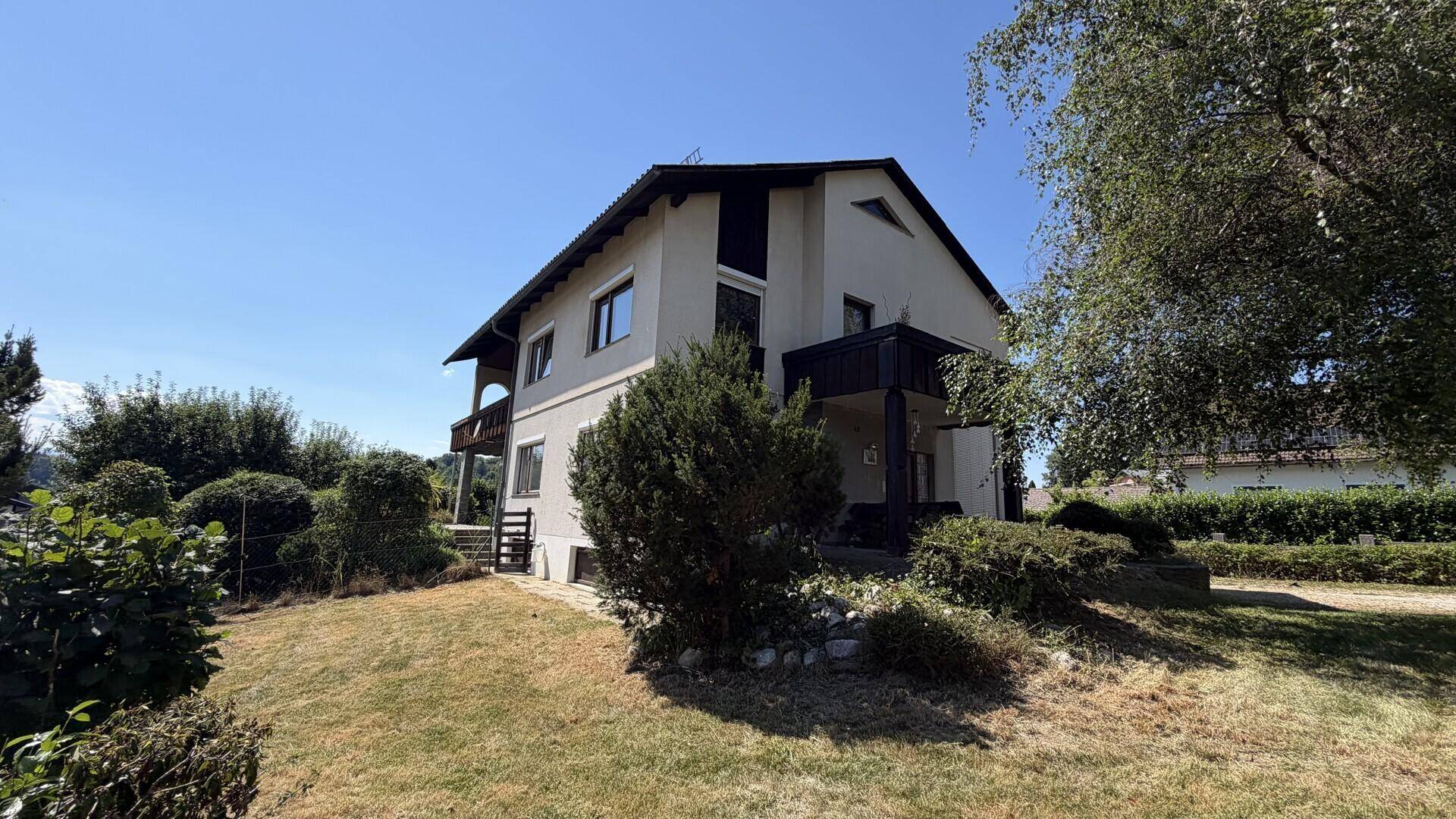 Hausansicht von der Seite mit gepflegtem Garten und Bäumen im Sommer.