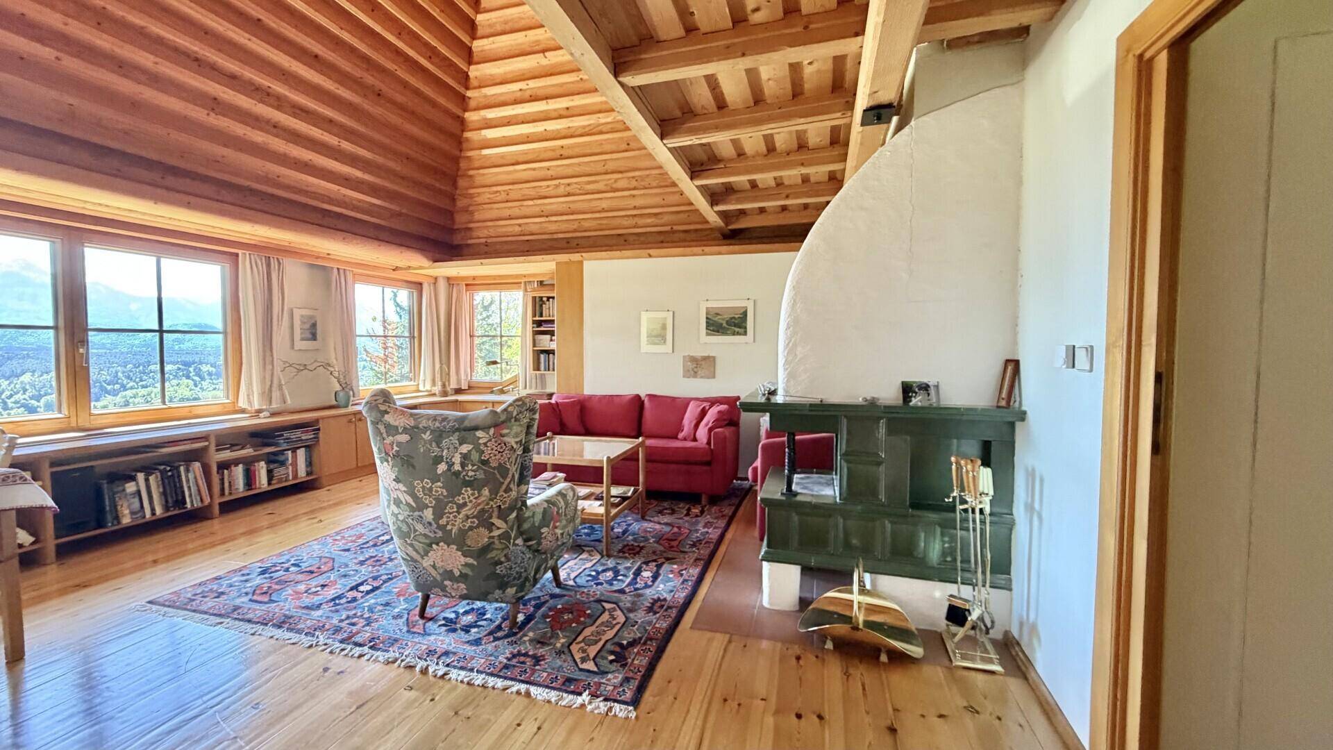 Großzügiges Wohnzimmer mit hoher Holzdecke, Kachelofen und Panoramablick auf die Berge.