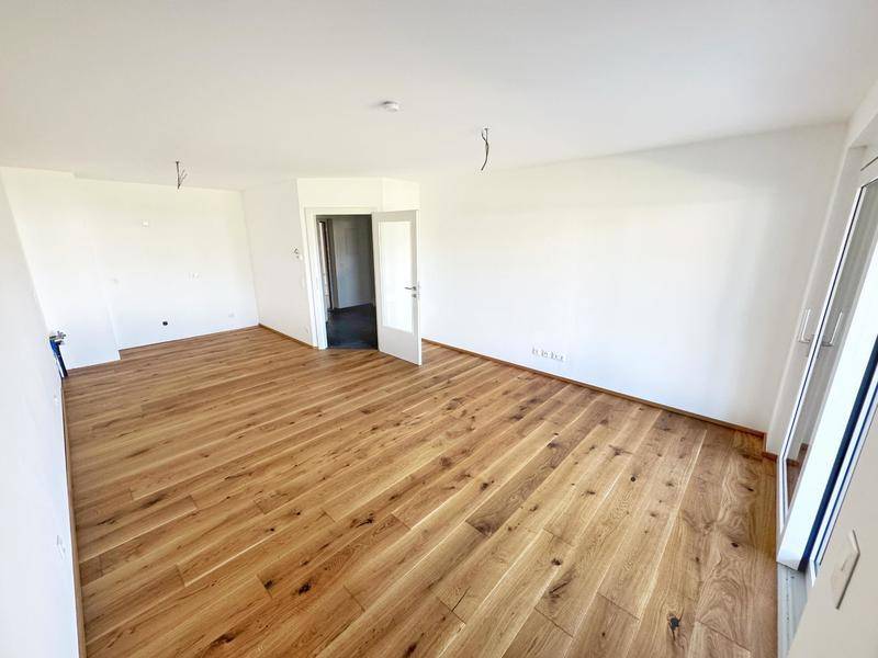 Lichtdurchfluteter Wohnbereich mit elegantem Holzboden und großen Fenstern, bereit zur Einrichtung.