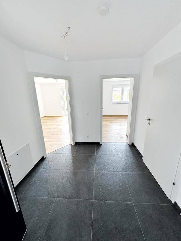 Heller Flur mit dunklen Fliesen und Zugang zu mehreren Zimmern in einer modernen Wohnung.