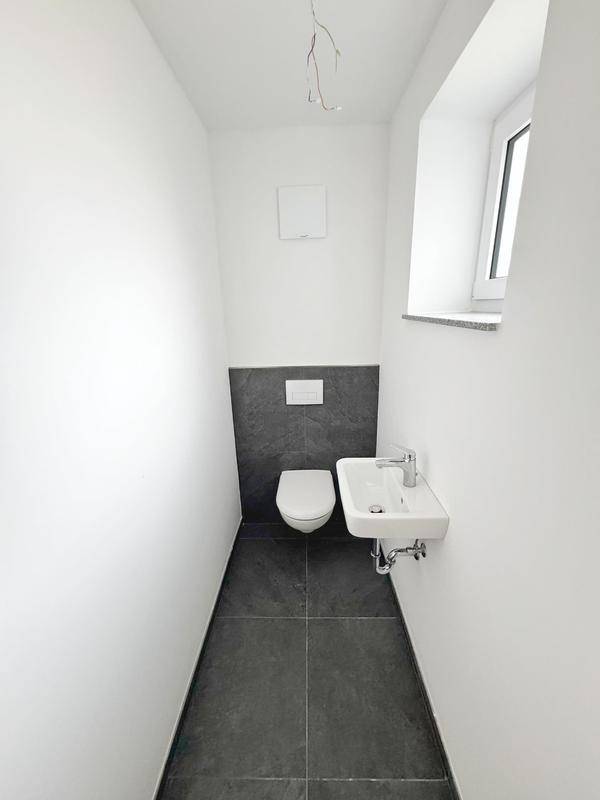 Modernes Gäste-WC mit dunklen Fliesen, wandhängendem WC und kleinem Waschbecken mit Fenster.
