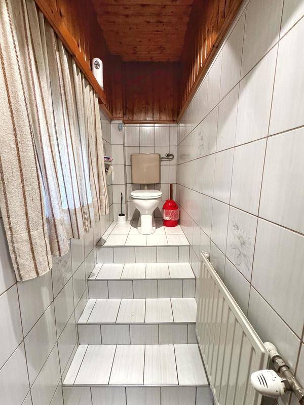 Kleines WC mit weißen Fliesen, Toilette auf einer erhöhten Stufe und Holzdecke.