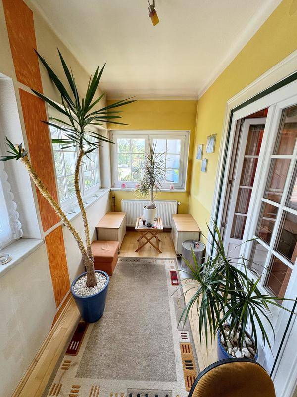 Heller Wintergarten mit vielen Pflanzen, Sitzgelegenheiten und gelben Wänden für entspannte Stunden.