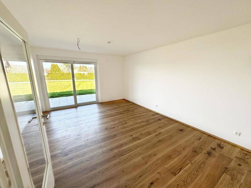 Heller, leerer Raum mit Holzboden und großem Schiebefenster zum Garten.