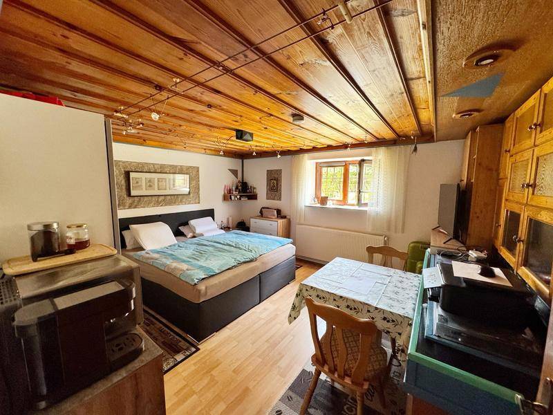 Gemütliches Schlafzimmer mit Holzbalkendecke, Doppelbett, Esstisch und kleiner Küchenzeile.