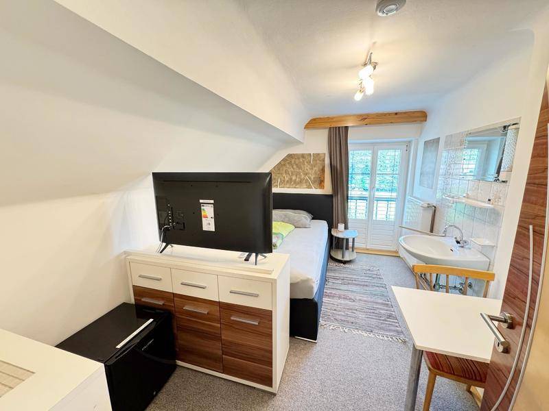 Schlafzimmer mit Dachschräge, Bett, Fernseher und integriertem Waschbecken.