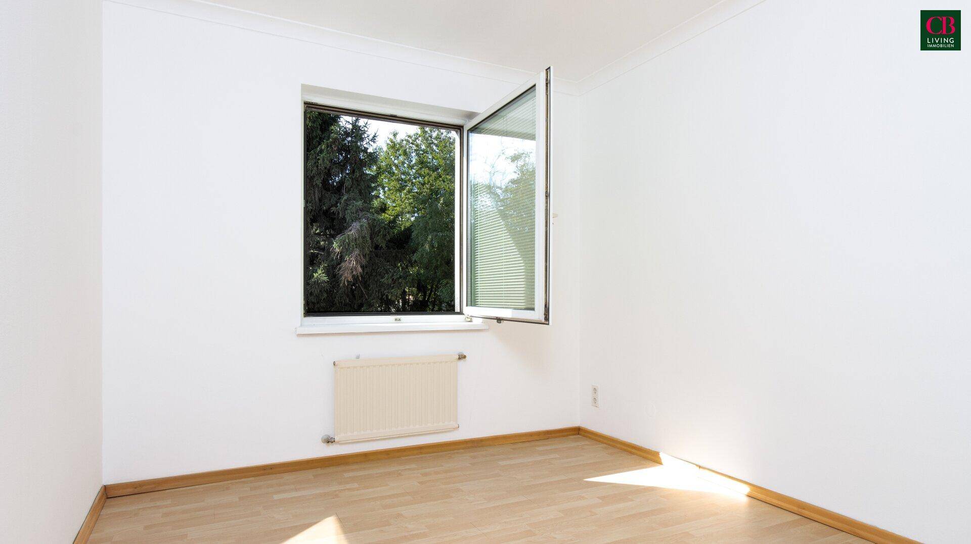 Lichtdurchflutetes Zimmer mit Parkettboden und großem, geöffnetem Fenster.