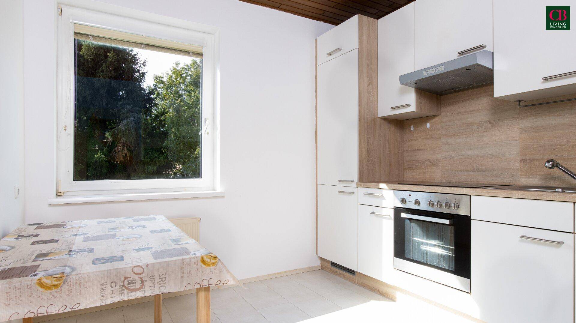 Helle Küche mit weißen Schränken, Holzakzenten und Fensterblick ins Grüne.