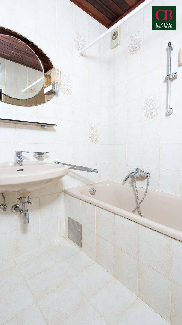 Badezimmer mit Badewanne, Waschbecken und hellen Fliesen im 80er-Jahre-Stil.