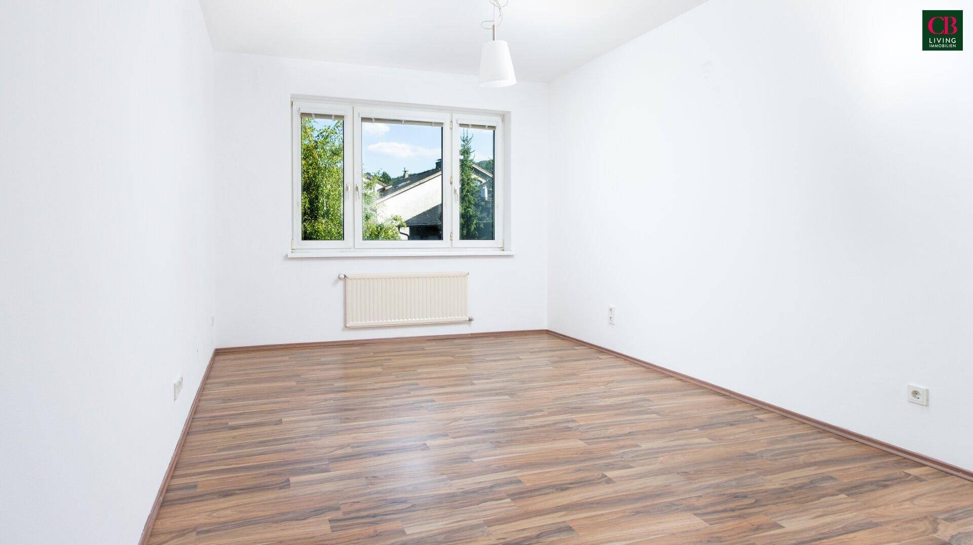 Geräumiges, helles Zimmer mit Laminatboden und großem Fenster mit Blick ins Grüne.