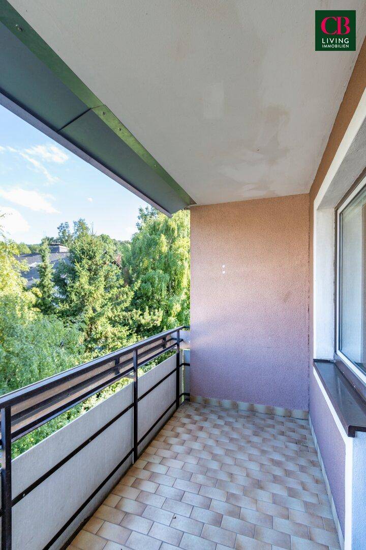 Heller Balkon mit Fliesenboden und Blick auf grüne Bäume und die Umgebung.