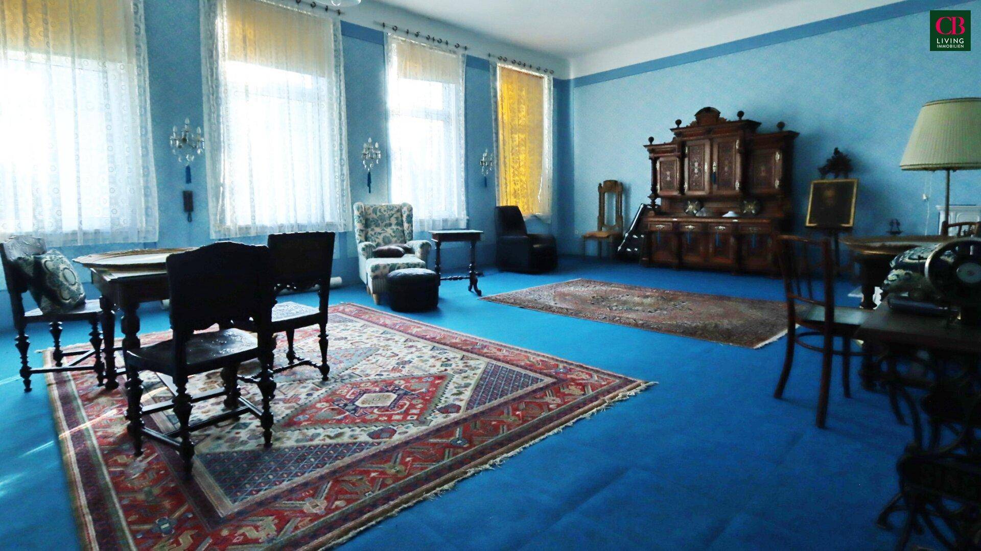 Geräumiger Salon mit blauer Wandfarbe, Teppichen und antiken Möbeln im klassischen Stil.
