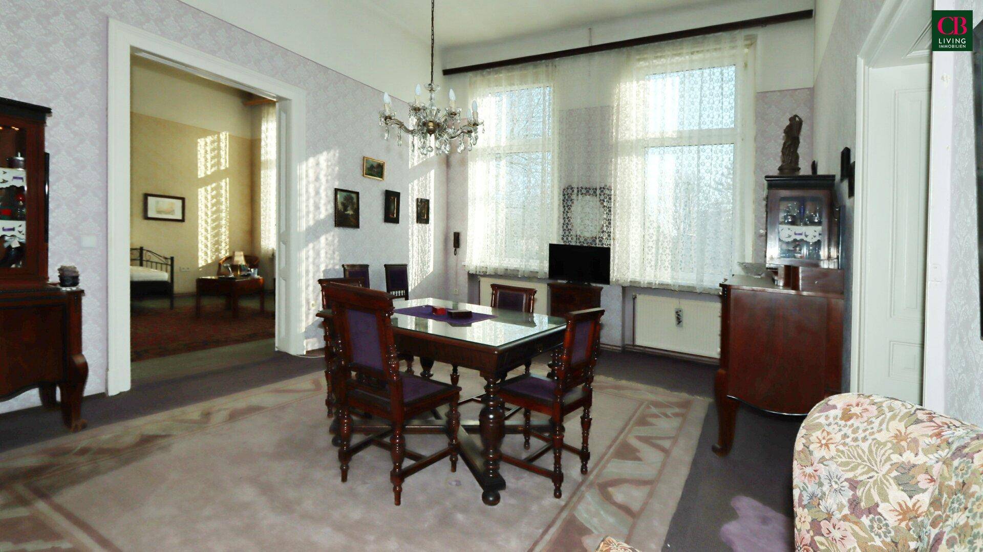 Klassischer Essbereich mit Kronleuchter, Holztisch und Zugang zu einem weiteren Zimmer.