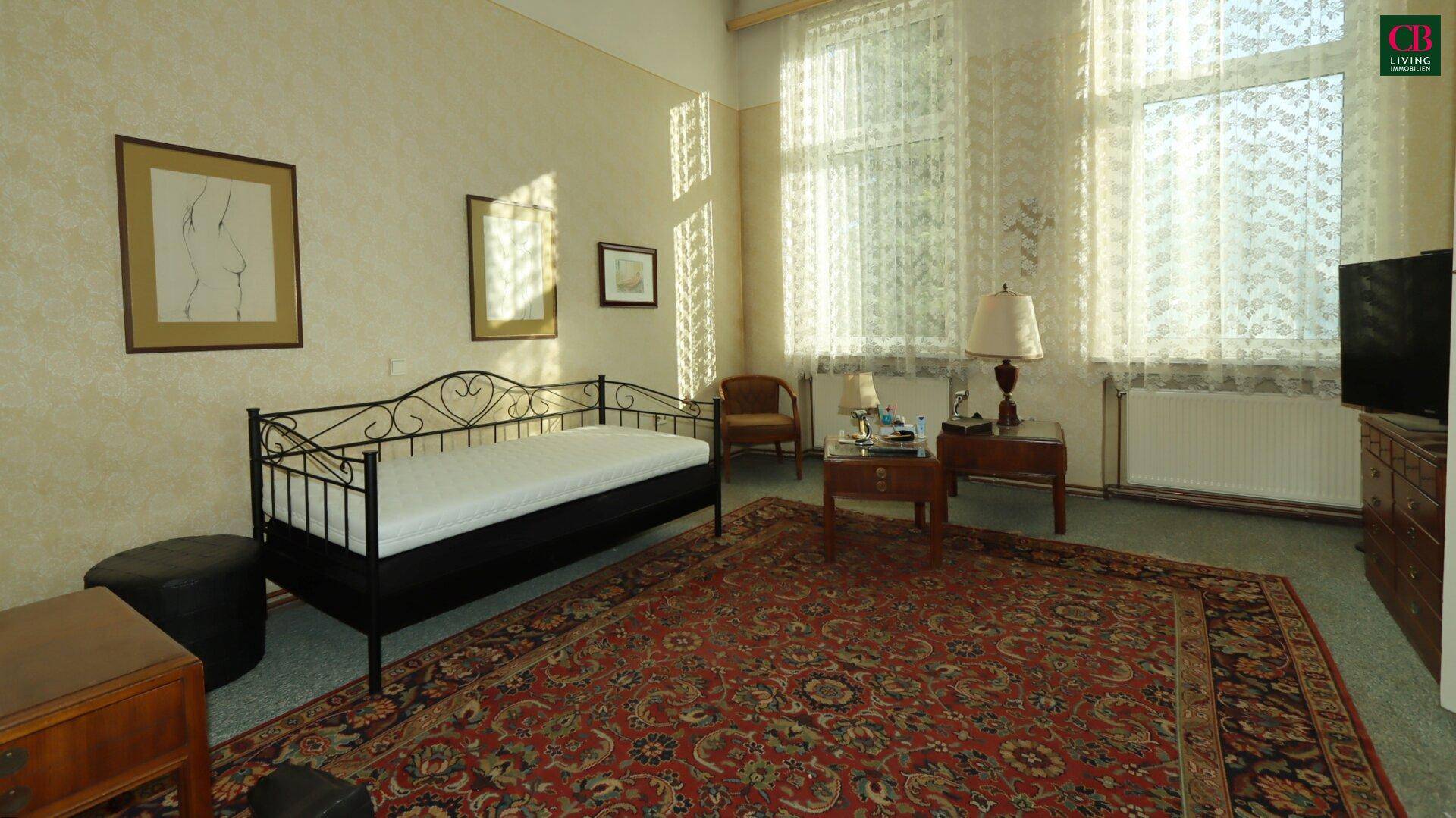 Helles Schlafzimmer mit Tagesbett, Teppichboden und großen Fenstern, die viel Licht hereinlassen.