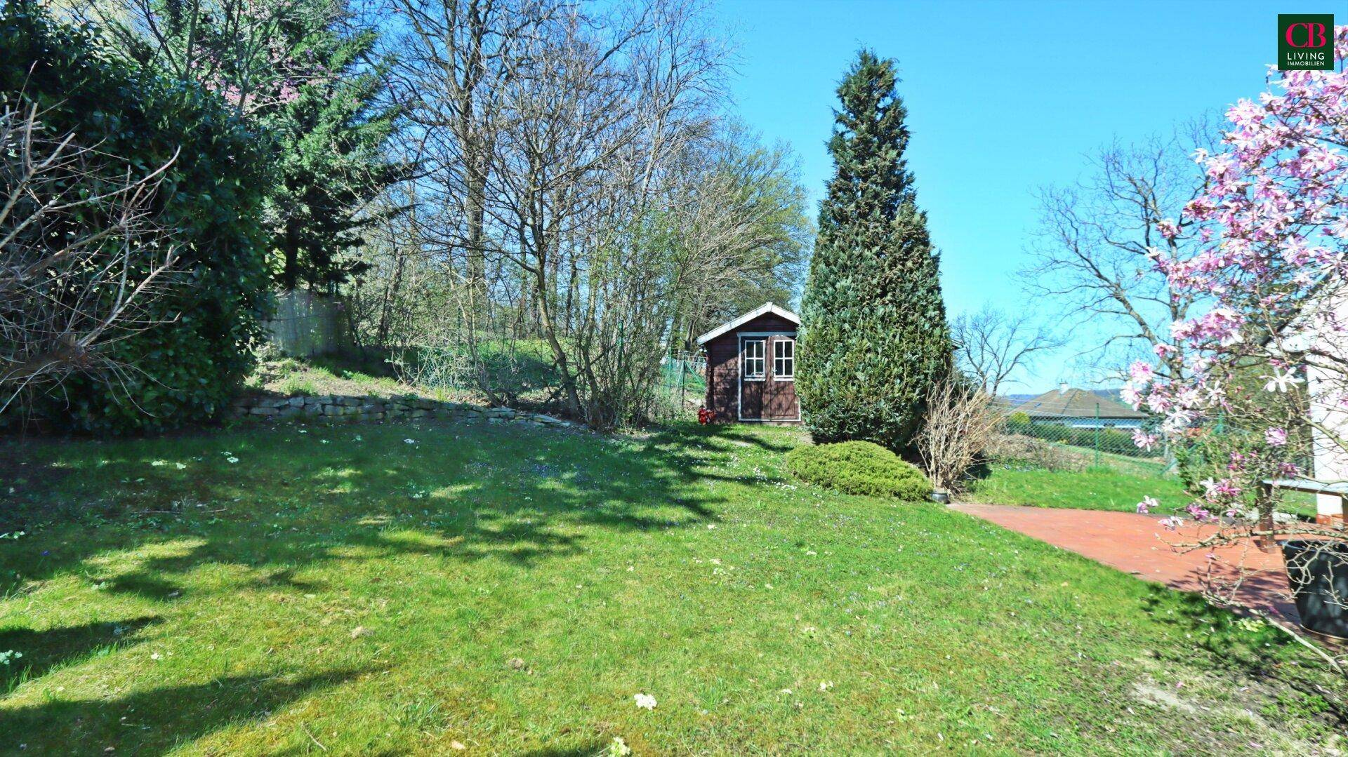 Gepflegter Gartenbereich mit Rasenfläche, Bäumen und einem kleinen Gartenhaus.