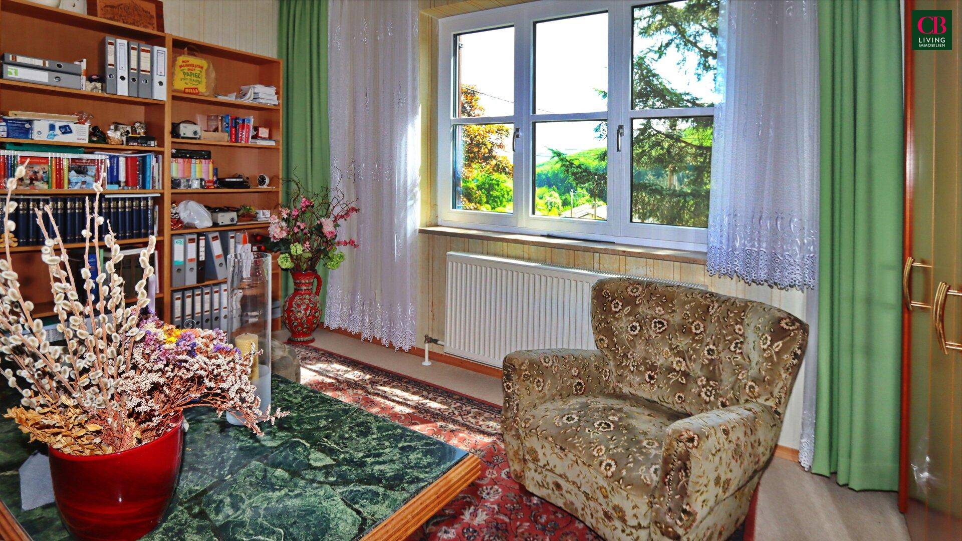 Helles Arbeitszimmer mit Bücherregal, Schreibtisch und Blick ins Grüne durch das Fenster.