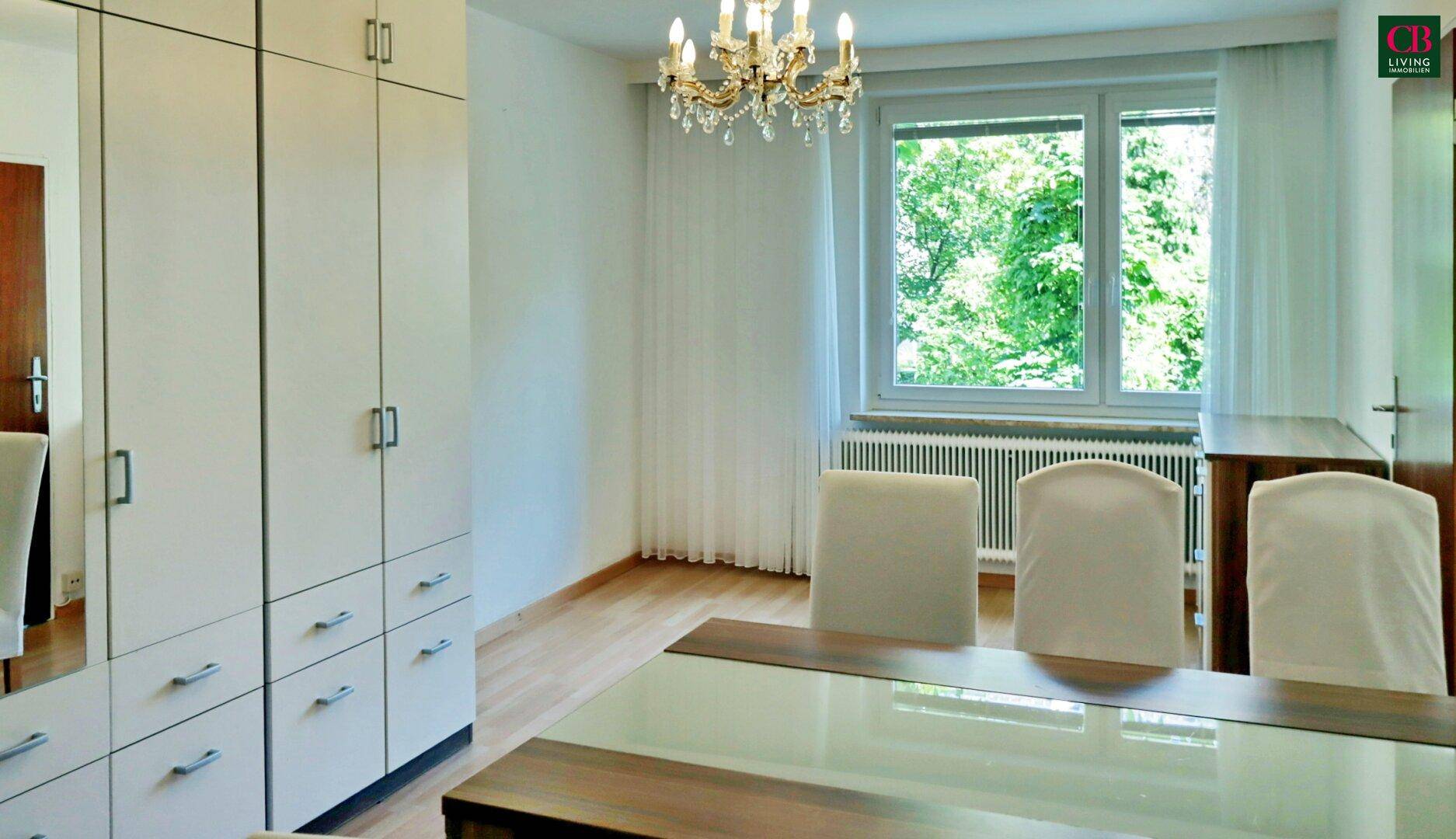 Heller Essbereich mit großem Fenster, Holzboden und Einbauschränken, bietet einen grünen Ausblick.