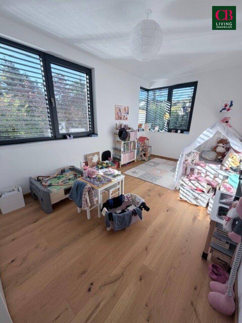 Helles Kinderzimmer mit Holzboden, großen Fenstern und Spielbereich, ideal für kleine Bewohner.