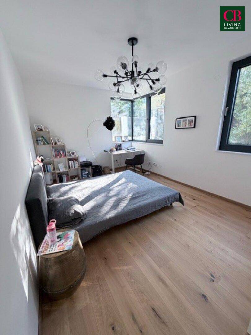 Gemütliches Schlafzimmer mit Holzboden, Schreibtisch und großem Fenster, das viel Licht hereinlässt.