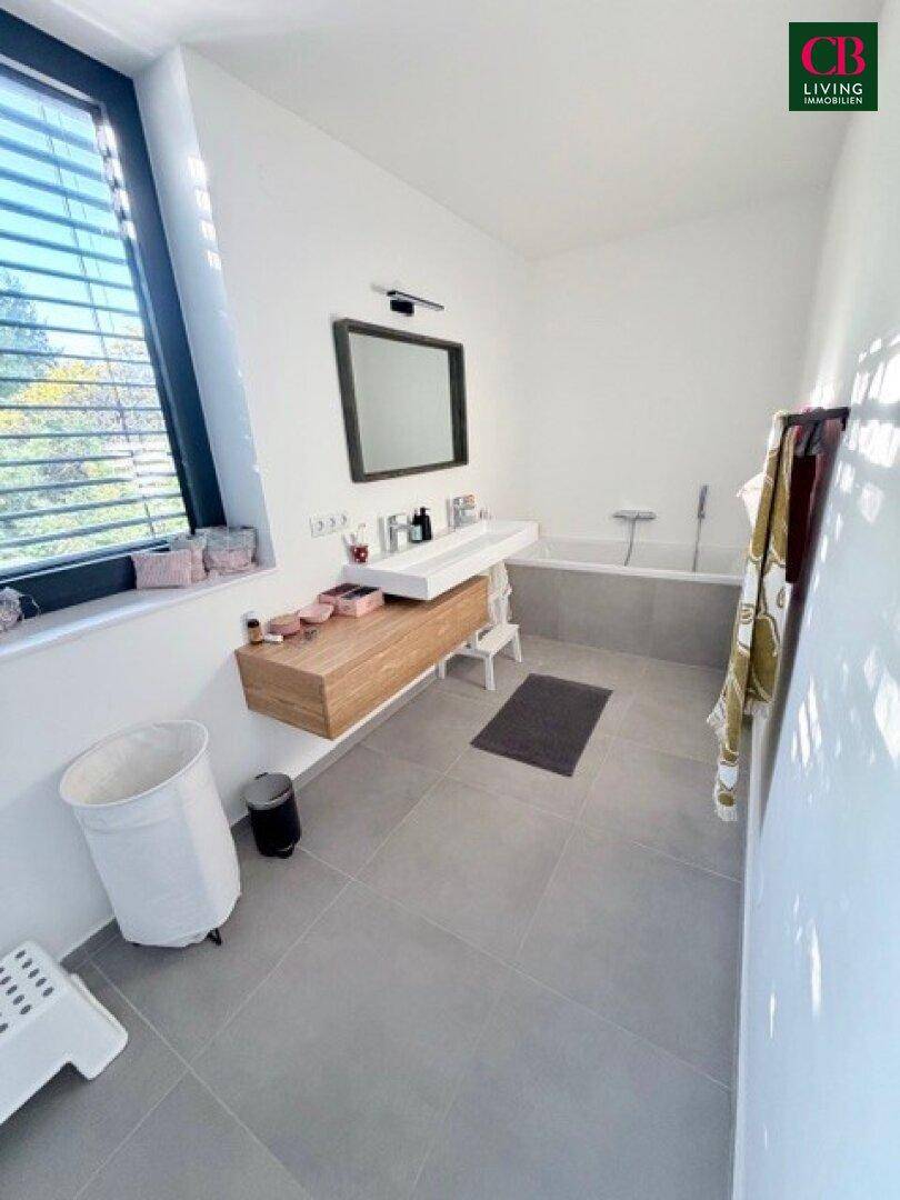 Helles Badezimmer mit Badewanne, Einzelwaschbecken und großem Fenster, das den Raum erhellt.