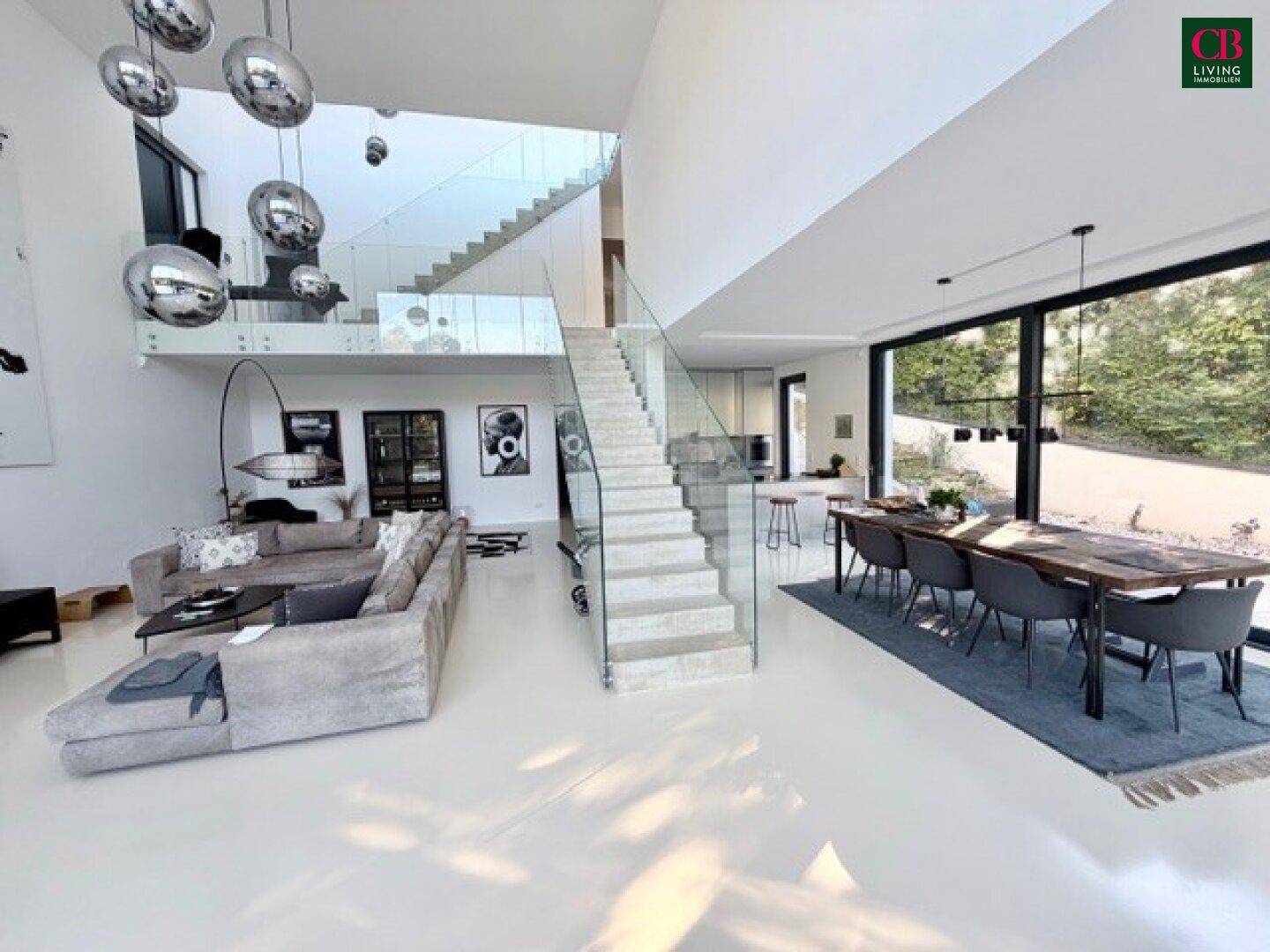 Lichtdurchfluteter Wohn-Essbereich mit eleganter Treppe, moderner Küche und Zugang zur Terrasse.
