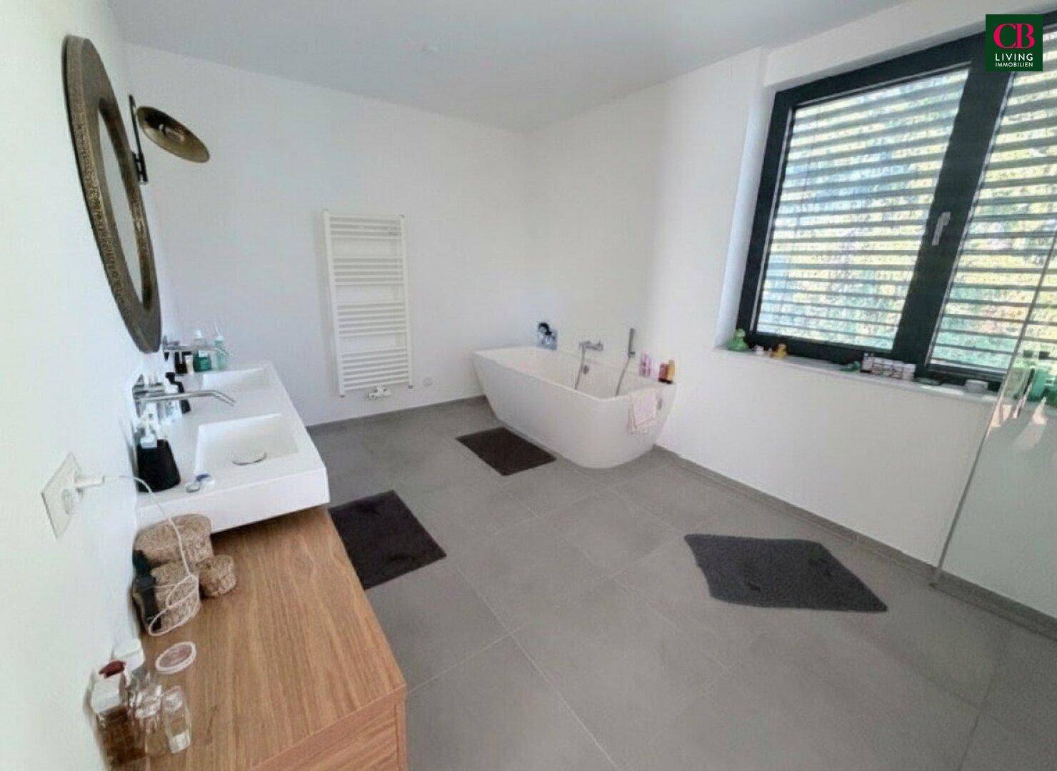 Modernes Badezimmer mit freistehender Badewanne, Doppelwaschbecken und großem Fenster für Tageslicht.