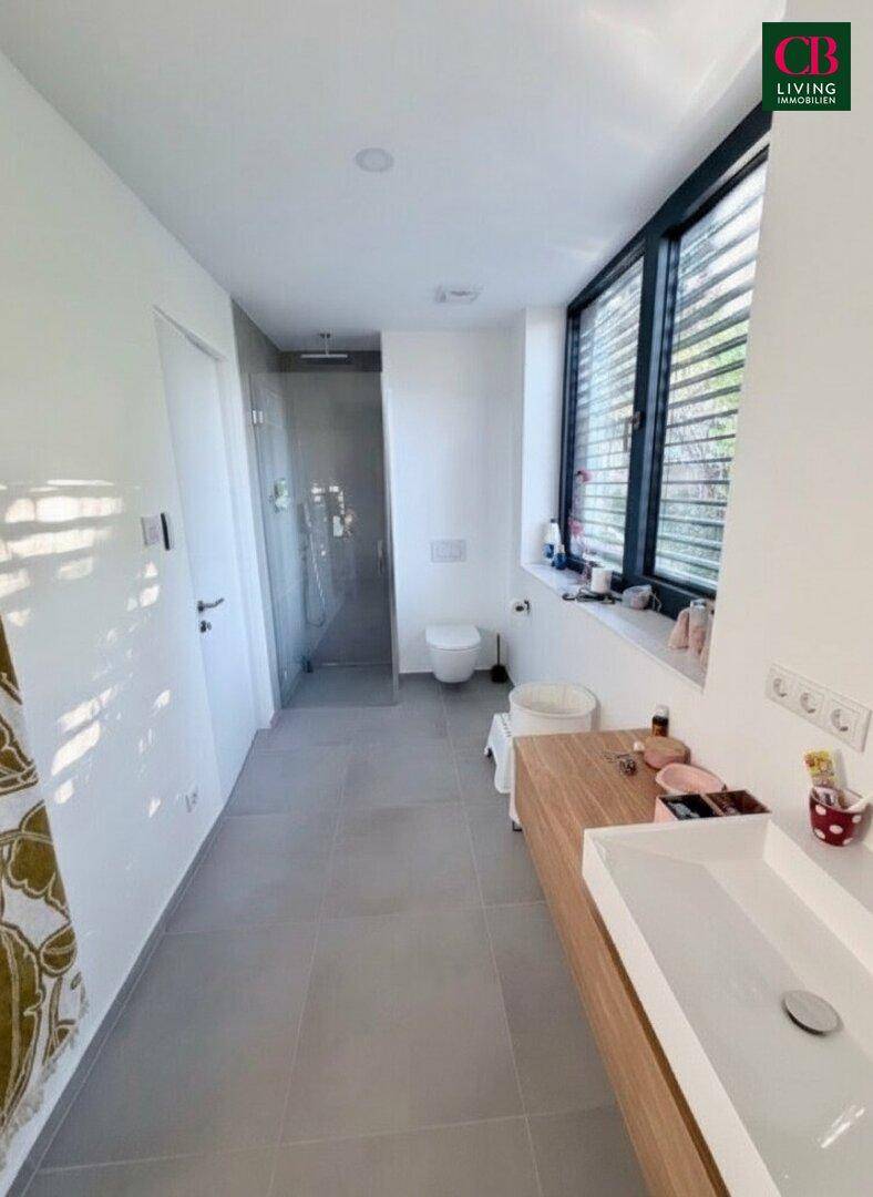 Modernes Badezimmer mit ebenerdiger Dusche, Wand-WC und großem Fenster für natürliche Belüftung.