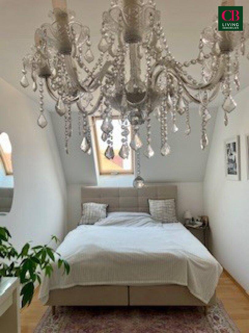 Gemütliches Schlafzimmer im Dachgeschoss mit Doppelbett, Holzboden und elegantem Kronleuchter.