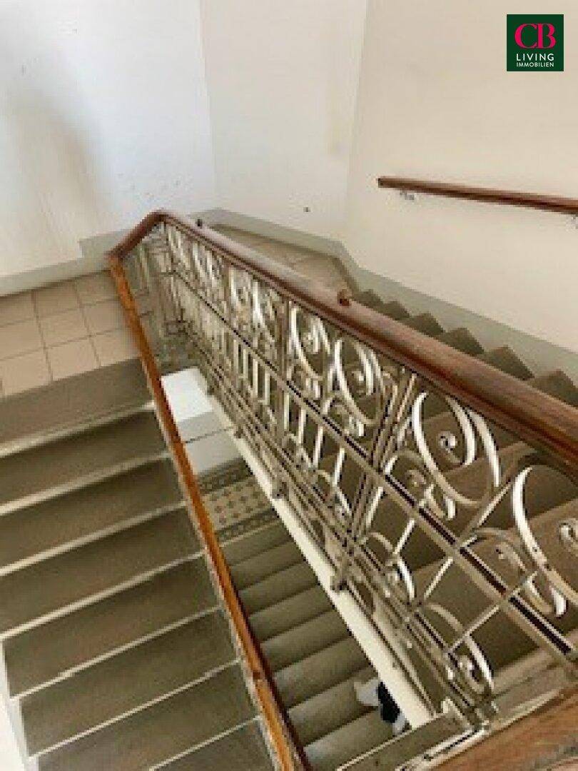 Historisches Treppenhaus mit kunstvollem Geländer und Fliesenboden im Eingangsbereich.