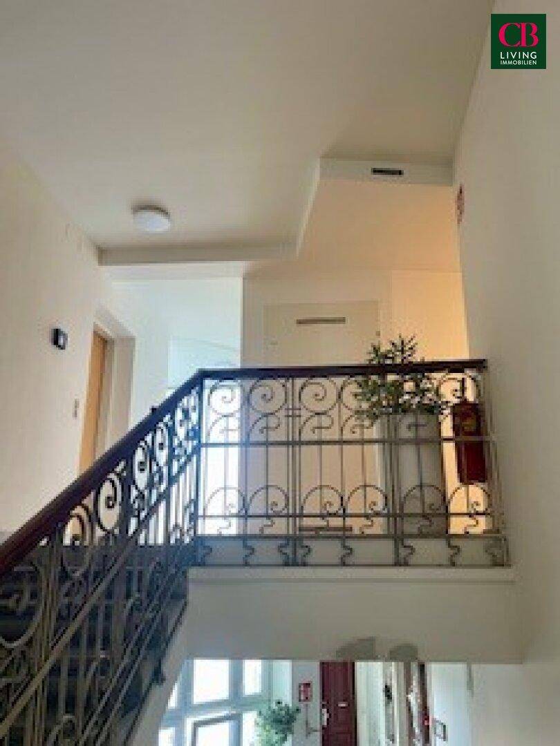 Elegantes Treppenhaus mit schmiedeeisernem Geländer und hohen Decken in einem Altbau.