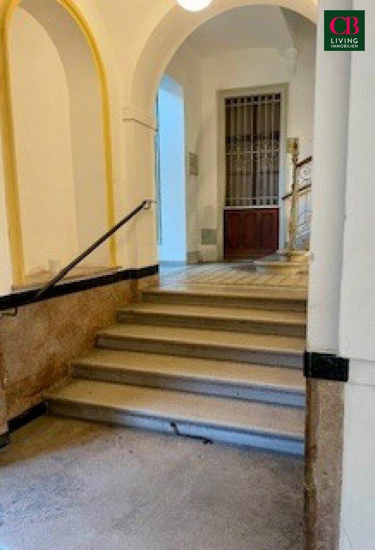 Historischer Eingangsbereich mit Steintreppe, Bögen und dekorativen Elementen.