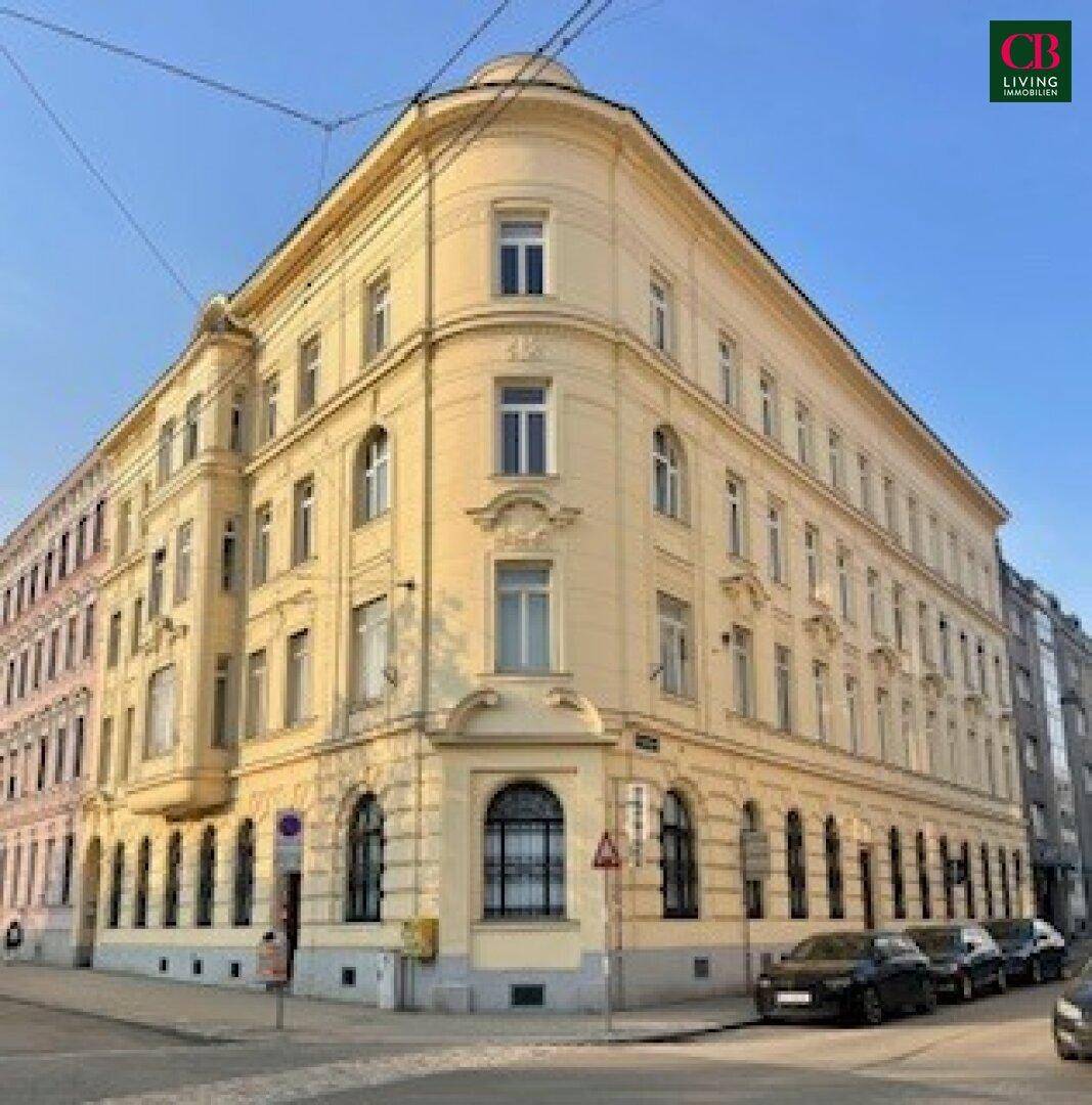 Historisches Eckgebäude mit eleganter Fassade und vielen Fenstern an einer Stadtstraße.