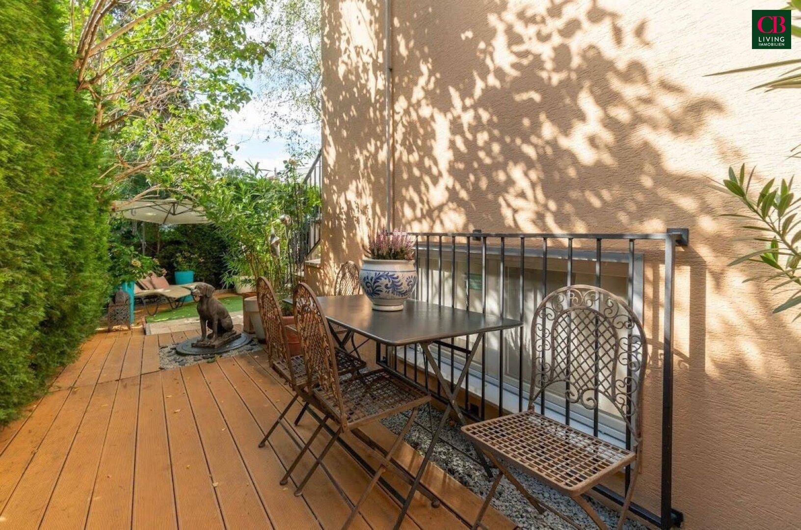 Holzterrasse mit schmiedeeisernen Gartenmöbeln und üppiger grüner Bepflanzung.